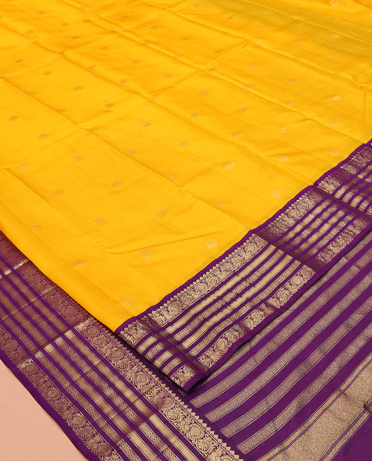 Yellow Vasundhara Silk Saree, Sparsely Woven with Zari Buttas All Over Its Body, Complemented by a Contrast Border of Thilakam, Muthu, Mayil, and Mayil Kann Designs, Pallu of Zari Designs, and Paired with a Contrast Blouse