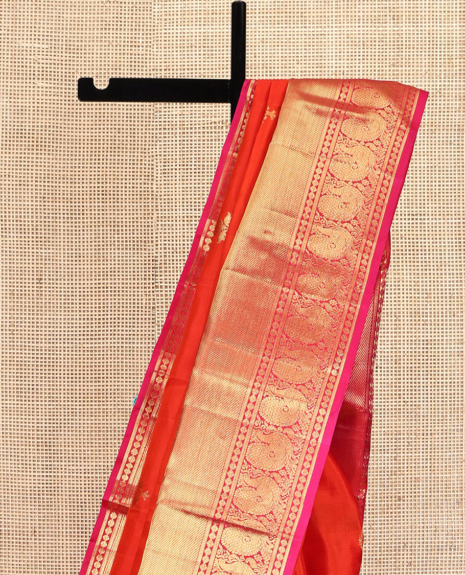Orange Kanchipuram Silk Saree, Bedecked with Zari Buttas All Over Its Body, Complemented by a Contrast Border of Manga Mokku, Poun, Yaanai, and Mayil Designs, Grand Pallu of Kodi Visiry Designs, and Paired with a Contrast Blouse