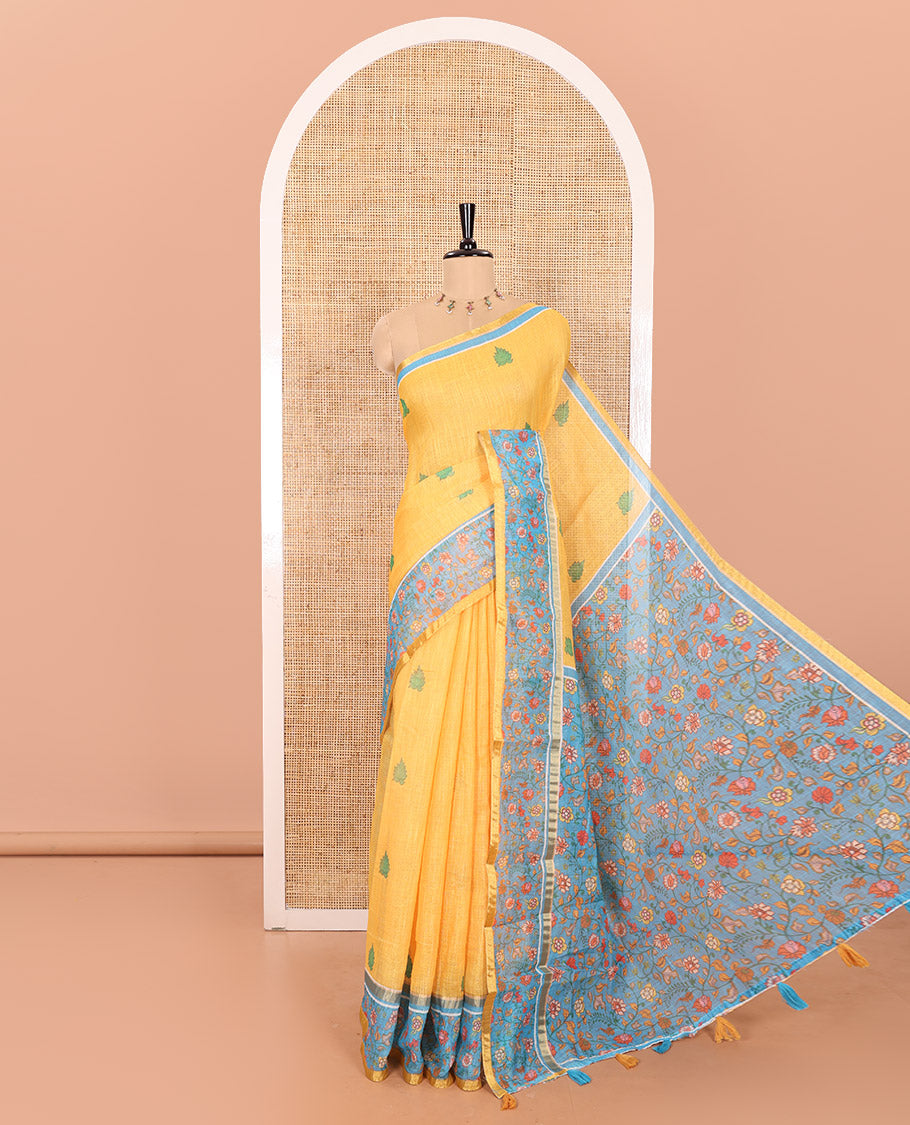 Yellow Linen Saree Detailed with Leaf Motifs All Over Its Body, Complemented by a Contrast Floral Vine Printed Border, Pallu Mirrors the Floral Vine Print, and Paired with a  Contrast Floral Printed Blouse