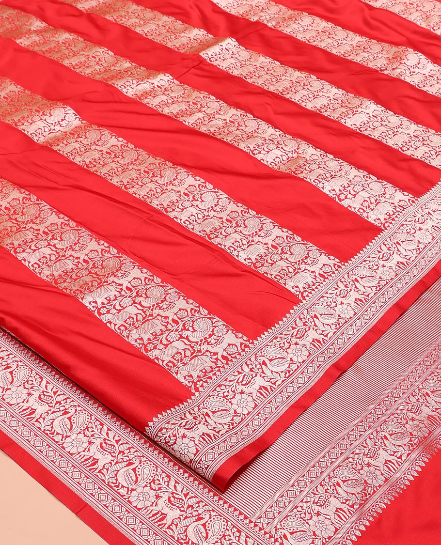 Red Mushuru Silk Saree, Gracefully Embellished with Vertically Woven Flora-Fauna Zari Designs On Its Body, Highlighted by Zari Border of Peacock and Deer Motifs, Grand Pallu, and Paired with a Plain Blouse