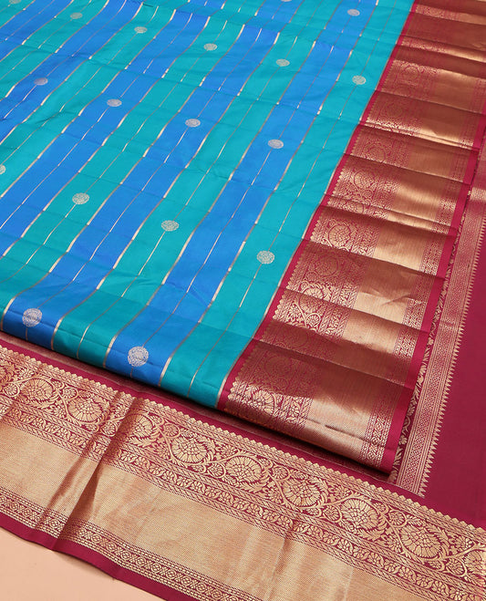 Blue Vasundhara Silk Saree, Impeccably Styled with Zari Buttas and Zari Stripes All Over Its Body, Complemented by a Contrast Border of Salngai, Puli Nagam, and Kodi Visiry Designs, Grand Gleaming Zari Woven Pallu, and Paired with a Contrast Blouse