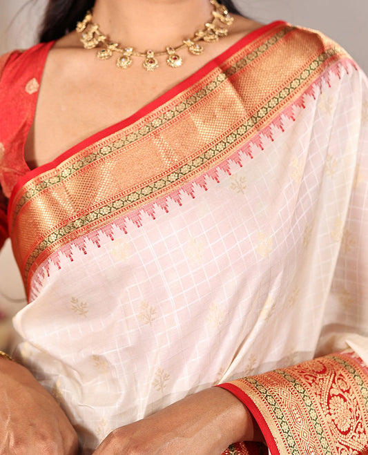 Cream Vasundhara Silk Saree, Subtly Sparkled with Buttas And Checks On Its Body, Complemented by Captivating Contrast Border of Thazampoo Rekku, Muthu, Banaras, and Kodi Visiry Designs, Pallu Steeped with Manga Designs, And Paired with a Contrast Blouse