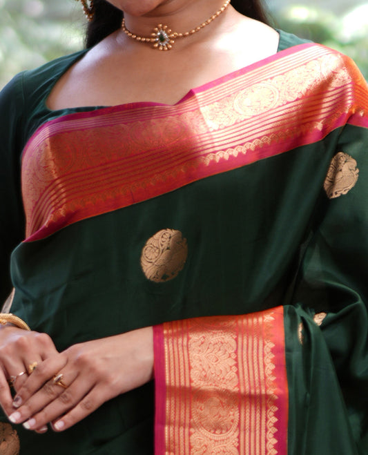 Green Vasundhara Silk Saree, Elevated with Mayil Zari Buttas All Over Its Body, Complemented by a Contrast  Border of Thilakam Mokku, Kathir, and Round Mayil Designs, Grand Jaal Pallu, and Paired with a Contrast Blouse