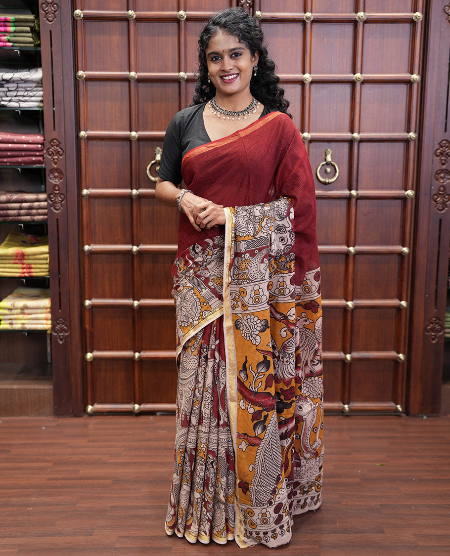 Maroon Kota Cotton Saree, Artfully Decked Up with Kalamkari-Style Human Figurines Printed on the Body, Subtle Piping Border, Pallu Pictures Kalamkari-Style Flora-Fauna Motifs, and Paired with a Contrast-Printed Blouse