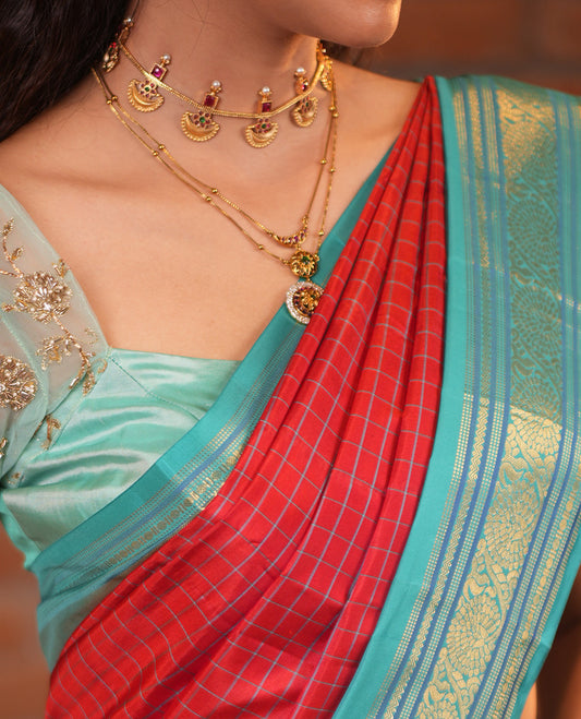 Tomato Red and Blue Vasundhara Silk Saree, Subtly Sparkled With Pattu Nool Kattam On Its Body, Complemented by Contrast Rettai Pettu Border of Salngai, Muthu, Neli, Rudraksham, and Dhavana Kodi Designs, Grand Pallu and Paired with a Contrast Blouse