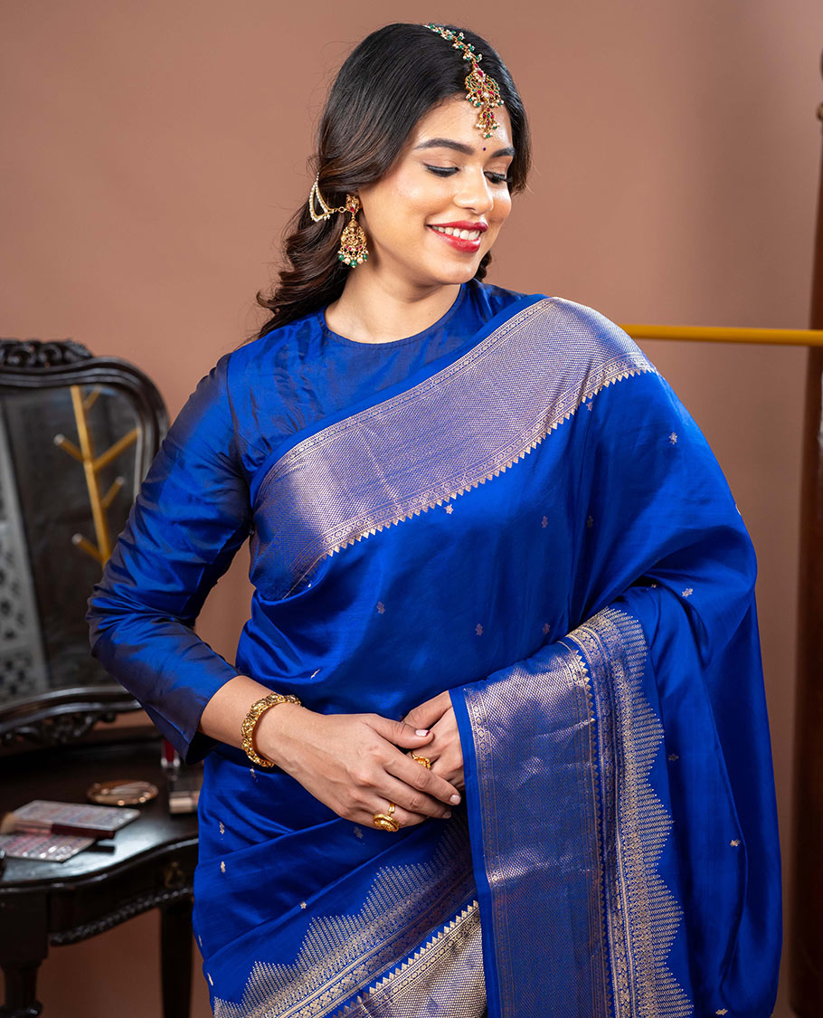 Blue Vasundhara Silk Saree Gleamed with Zari Buttas All Over Its Body, Highlighted with a Zari Border of Thilakam Mokku, Muthu, Cross Kamalam, and Mayil Kann Designs, Grand Pallu of Jaal Design, and Paired with a Matching Blouse