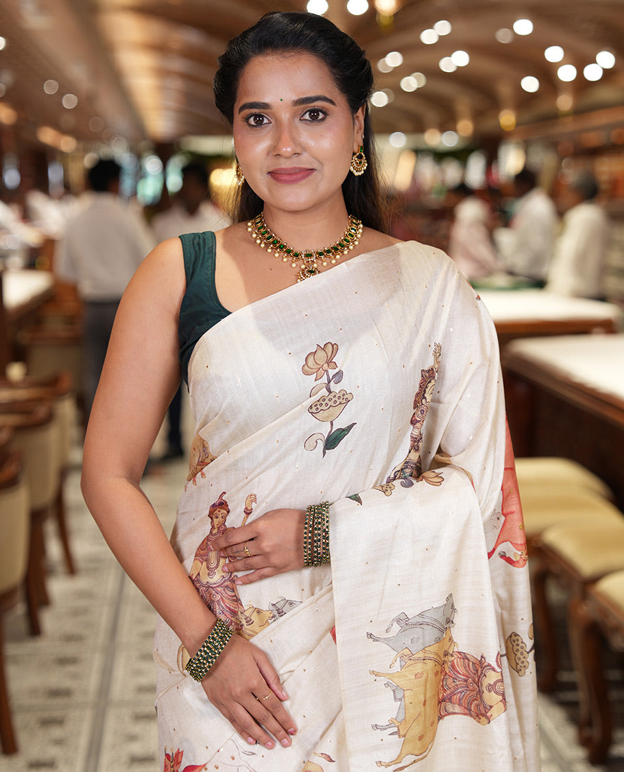 Borderless Cream Semi-Tussar Saree, Artfully Printed with Ancient Human Figurines, Floral, and Pichwai Cow on Its Body, Highlighted by Kalamkari-Style Human Motifs Printed Pallu, and Paired with a Matching Pichwai Cow Printed Blouse