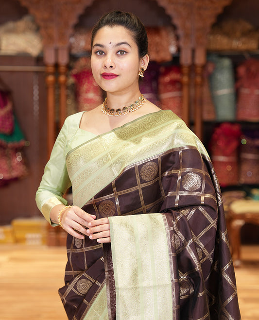 Coffee Brown and Elaichi Green Litchi Saree Elegantly Decked up with Chakra Butta Enclosed Zari Checks, Complemented by a Contrast Border Steeped with Chakram Motifs, Pallu Featuring Intricate Designs, and Comes with a Contrast Blouse
