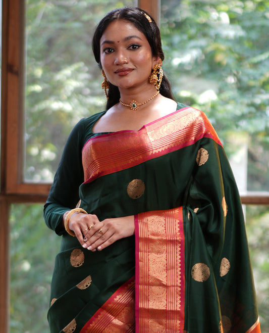 Green Vasundhara Silk Saree, Elevated with Mayil Zari Buttas All Over Its Body, Complemented by a Contrast  Border of Thilakam Mokku, Kathir, and Round Mayil Designs, Grand Jaal Pallu, and Paired with a Contrast Blouse