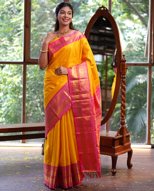 Mango Yellow Vasundhara Silk Saree, Subtly Sparkled with Sparse Stripes and Zari Buttas, Complemented by a Contrast Border of Thilakam, Banaras, Muthu, and Round Mayil Designs, Pallu Steeped with Traditional Designs, and Paired with a Contrast Blouse