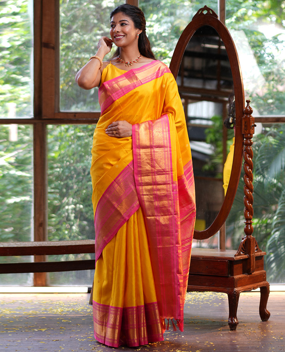 Mango Yellow Vasundhara Silk Saree, Subtly Sparkled with Sparse Stripes and Zari Buttas, Complemented by a Contrast Border of Thilakam, Banaras, Muthu, and Round Mayil Designs, Pallu Steeped with Traditional Designs, and Paired with a Contrast Blouse