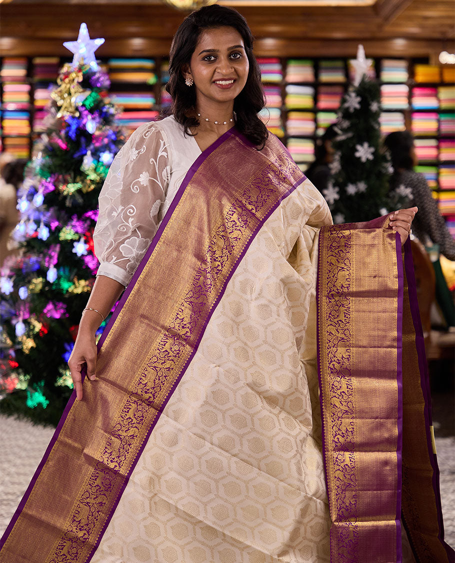 Cream jacquard silk saree, contrast vanasingaram style border of thilakam mokku, kodi visiry, mayil, maan, and yaanai designs, and intricate pallu