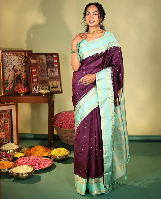 Purple Vasundhara Silk Saree, Spotlighted With Zari Buttas All Across Its Body, Complemented by Captivating Contrast Rettai Pettu Border of Thazampoo Rekku, Muthu, And Manga Designs, a Gleaming Zari Design Pallu, And Paired With a Contrast Blouse