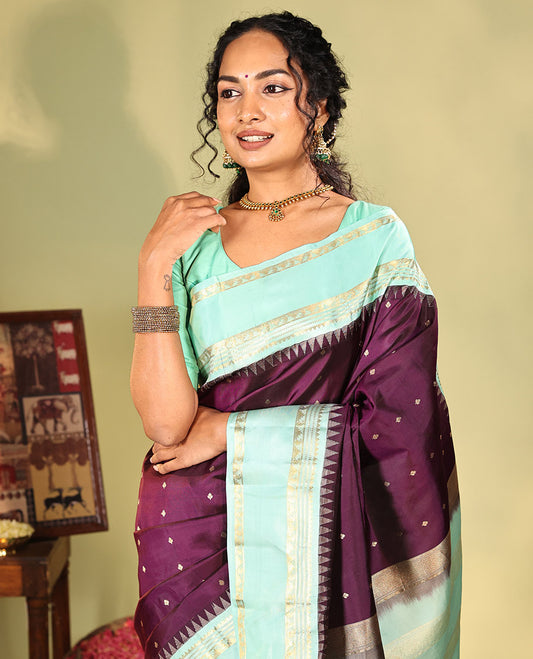 Purple Vasundhara Silk Saree, Spotlighted With Zari Buttas All Across Its Body, Complemented by Captivating Contrast Rettai Pettu Border of Thazampoo Rekku, Muthu, And Manga Designs, a Gleaming Zari Design Pallu, And Paired With a Contrast Blouse