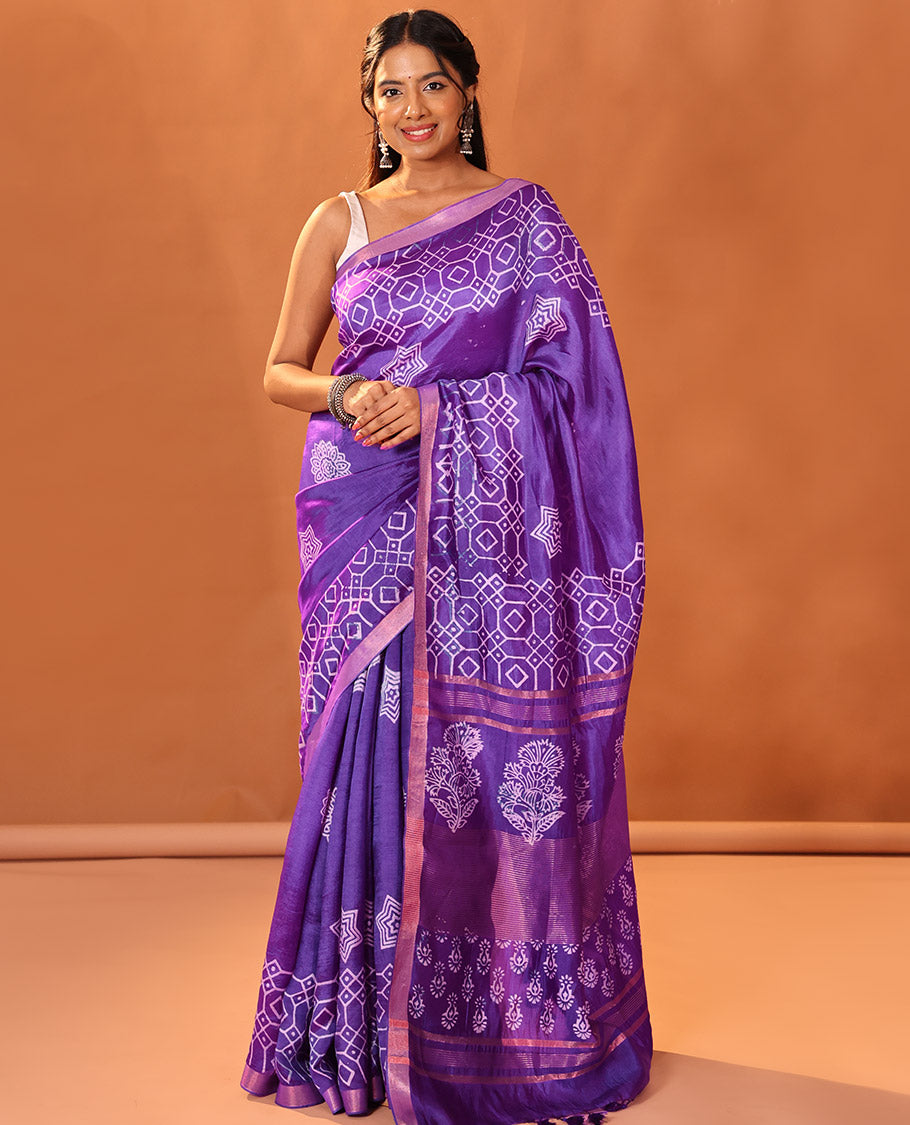 Purple Banana Pith Gleamed Up with Batik-Style Star and Kolam Motifs Printed All Over Its Body, Subtly Woven Zari Piping Border, Pallu Depicts Floral Motifs Block Print, and Gleaming Zari Stripes, and Paired with a Contrast Blouse