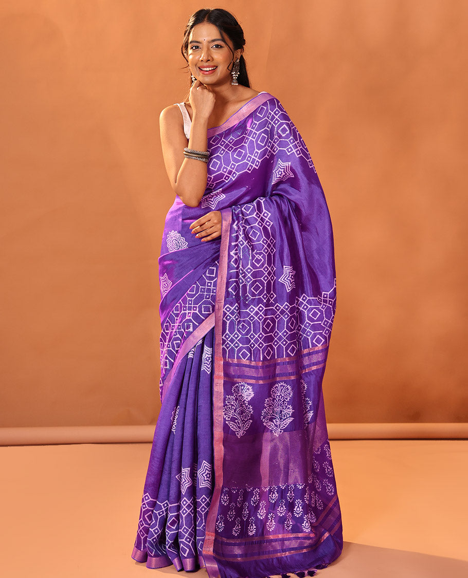 Purple Banana Pith Gleamed Up with Batik-Style Star and Kolam Motifs Printed All Over Its Body, Subtly Woven Zari Piping Border, Pallu Depicts Floral Motifs Block Print, and Gleaming Zari Stripes, and Paired with a Contrast Blouse