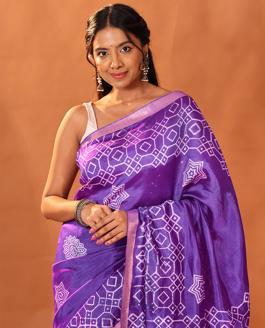 Purple Banana Pith Gleamed Up with Batik-Style Star and Kolam Motifs Printed All Over Its Body, Subtly Woven Zari Piping Border, Pallu Depicts Floral Motifs Block Print, and Gleaming Zari Stripes, and Paired with a Contrast Blouse
