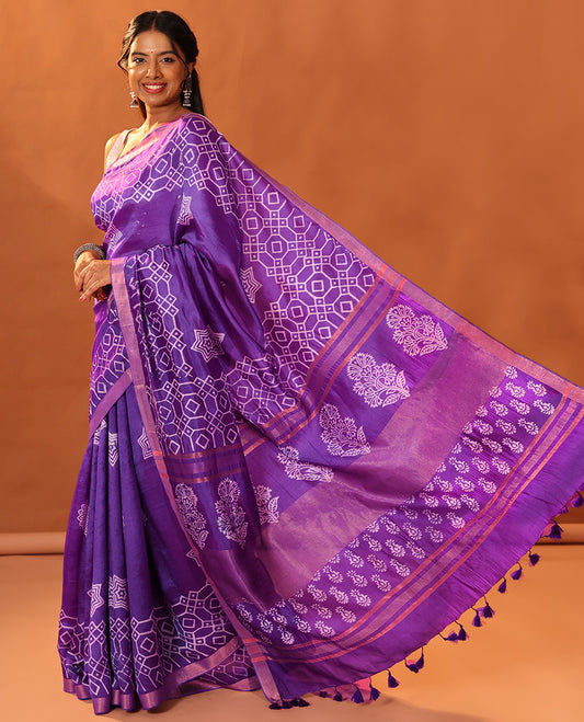 Purple Banana Pith Gleamed Up with Batik-Style Star and Kolam Motifs Printed All Over Its Body, Subtly Woven Zari Piping Border, Pallu Depicts Floral Motifs Block Print, and Gleaming Zari Stripes, and Paired with a Contrast Blouse