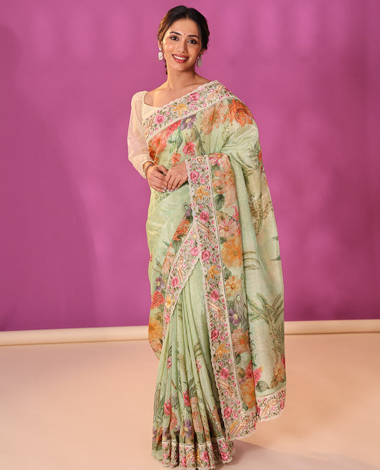 Green Dola Saree Gleamed Up with Gold Buttas and Colorful Tropical Floral Printed All Over Its Body, Complemented by a Contrast Scallop Floral Thread Embroidery Border, Pallu Depicts the Same Body Designs, and Paired with a Contrast Blouse