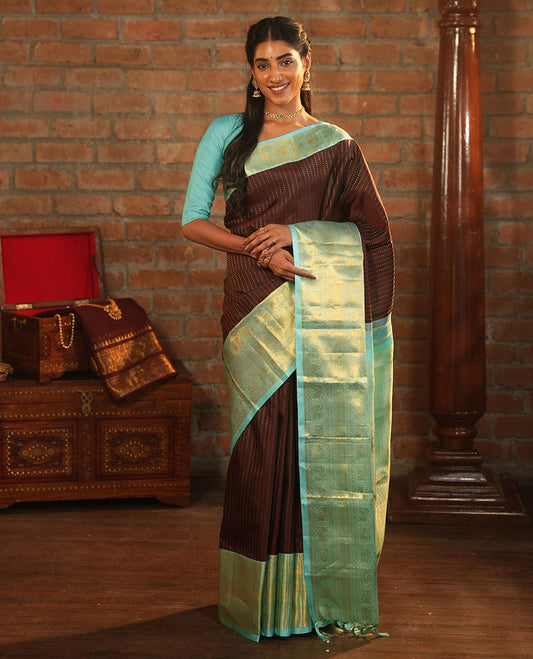 Brown Vasundhara Silk Saree Delicately Woven with Zari Buttas, Highlighted with a Contrast Border of Cross Kamalam, Mayil, Banaras, Yaanai, and Mayil Kann Designs, Pallu Grandly Woven with Jaal Designs, and Paired with a Contrast Blouse