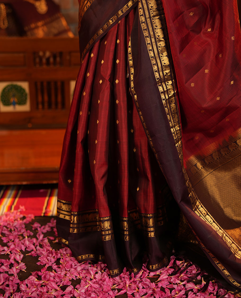 Maroon Vasundhara Silk Saree Decorated with Zari Buttas All Over Its Body, Complemented by a Contrast Rettai Pettu Border Steeped with Yaanai Motifs, Richly Detailed Pallu of Jaal Designs, and Paired with a Contrast Zari Bordered Blouse