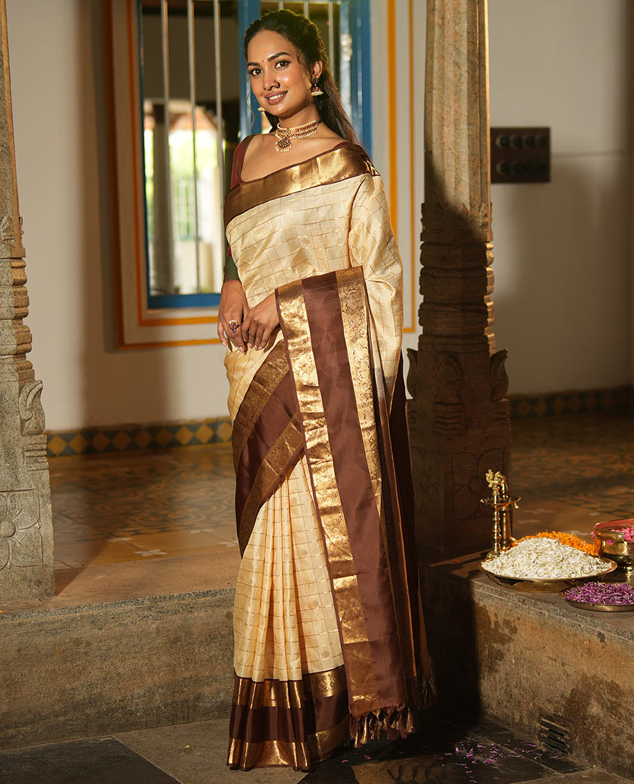Cream Vasundhara Silk Saree, Enthralled with Zari Buttas Enclosed Checks All Over Its Body, Complemented by a Contrast Rettai Pettu Border of Muthu, Banaras, and Iruthalai Pakshi Designs, a Grand Pallu, and Paired with a Contrast Blouse